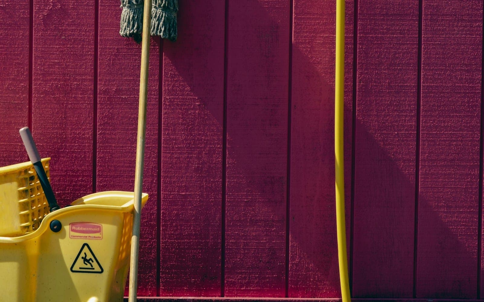 Mop, cleaning handle and yellow wringer bucket against a wall.