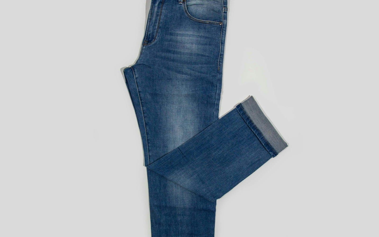 Blue denim jeans with a folded leg on a light background.