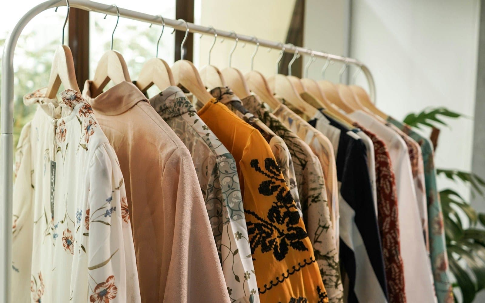 Assorted patterned blouses and tops displayed on wooden hangers.