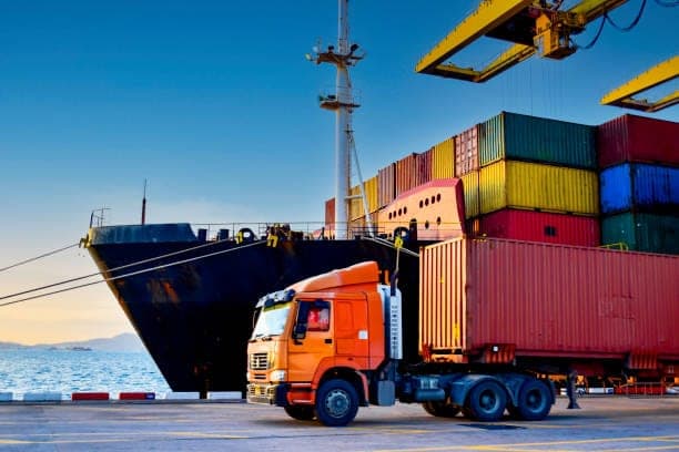 Container truck beside a cargo ship and stacked containers at a port; temporary sourcing and logistics image.