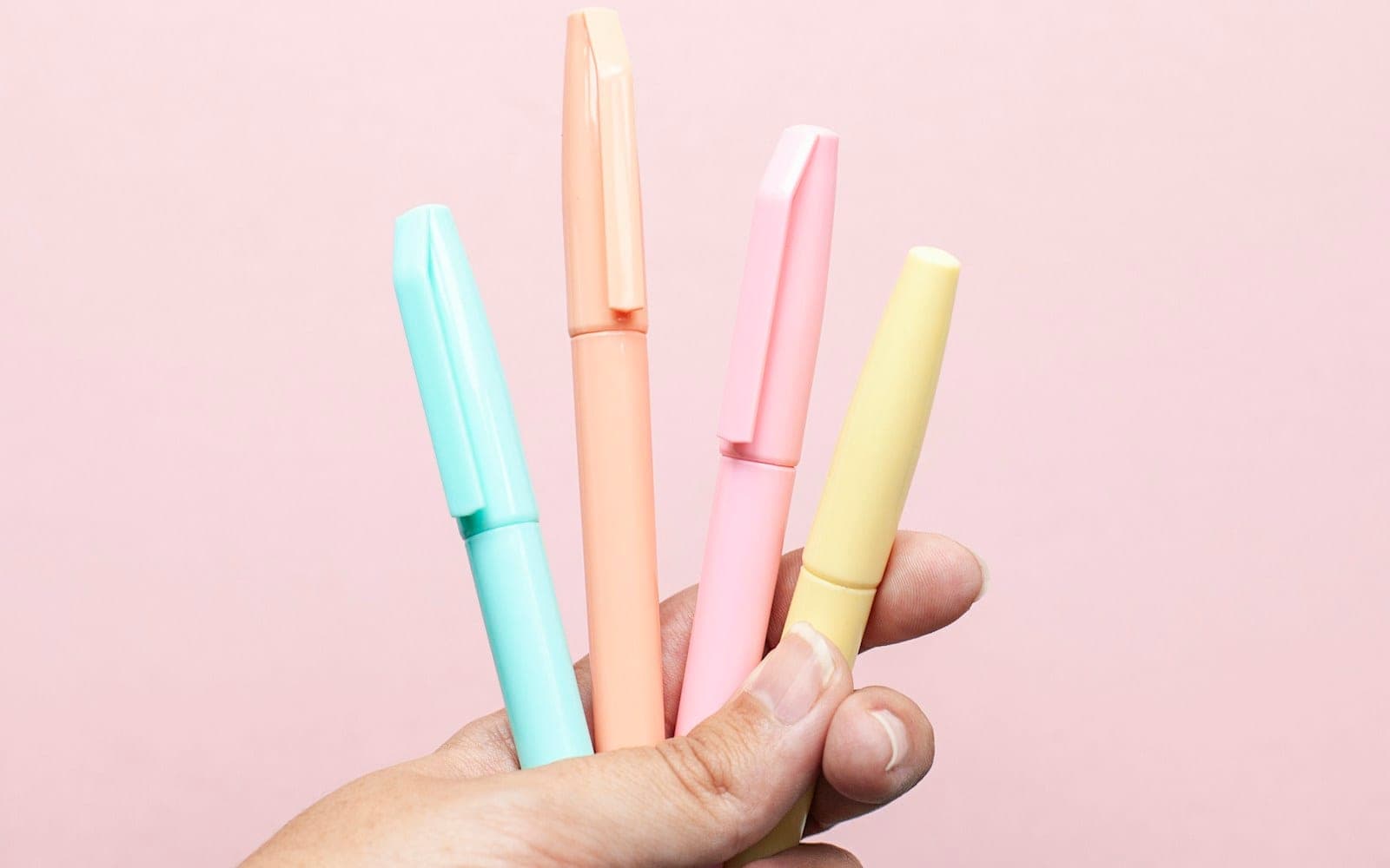 Four pastel-coloured highlighter pens held against a pink background.