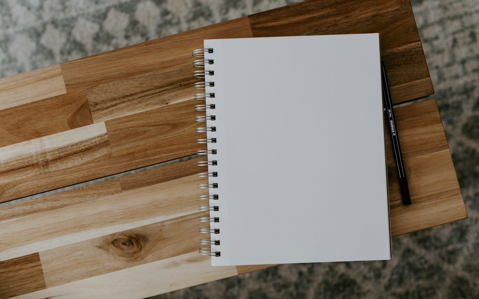 White spiral notebook and pencil on a wooden surface.