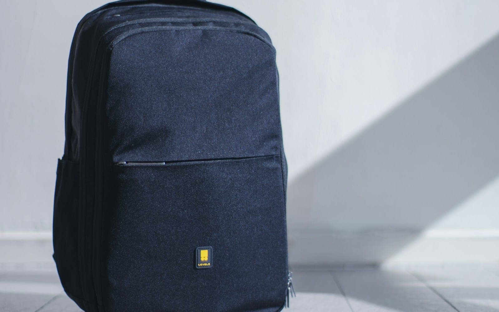 A black backpack with a small yellow logo on a white floor