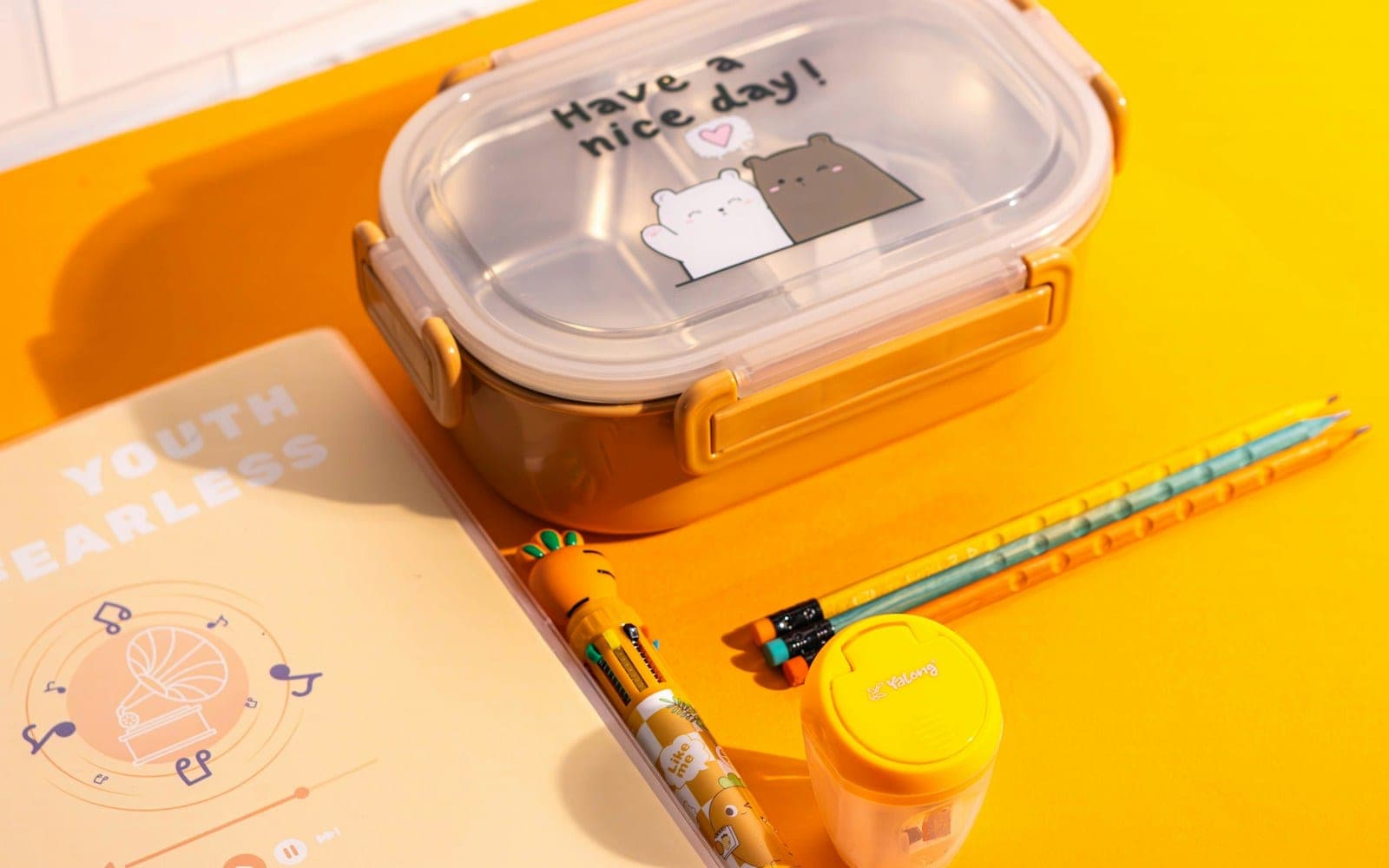 Reusable lunch box with a clear lid and side clips on a yellow desk.